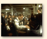 Hier speelt de pianist, in alle opzichten iets minder formeel, voor personeel en passagiers van de dieperliggende scheepsdekken van de Virginian in de film 'Legend of 1900'